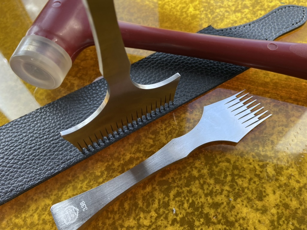 Процес ручної роботи зі шкірою: сталеві пробійники, нейлоновий молоток і темно-синя текстурована шкіра на робочій поверхні.